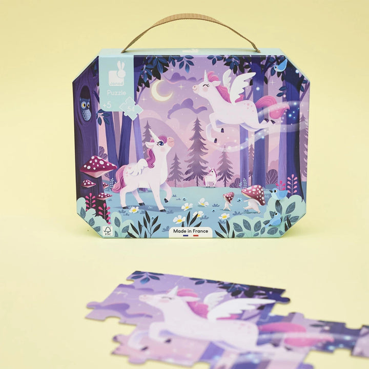 Koffer des Janod Einhörner-Puzzles mit losen Puzzleteilen auf gelbem Untergrund.