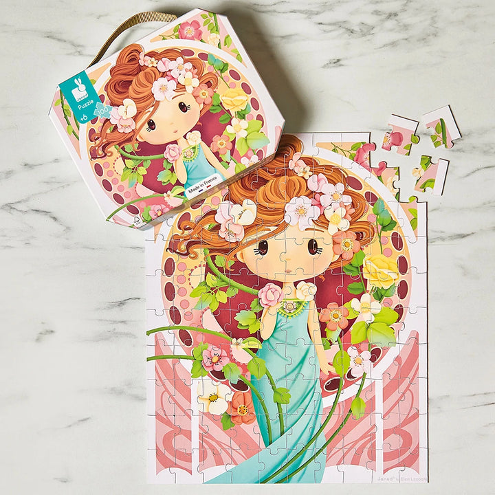 Janod Puzzle inspiriert von Mucha beim Zusammensetzen, mit Koffer und losen Teilen auf einer Marmorfläche.