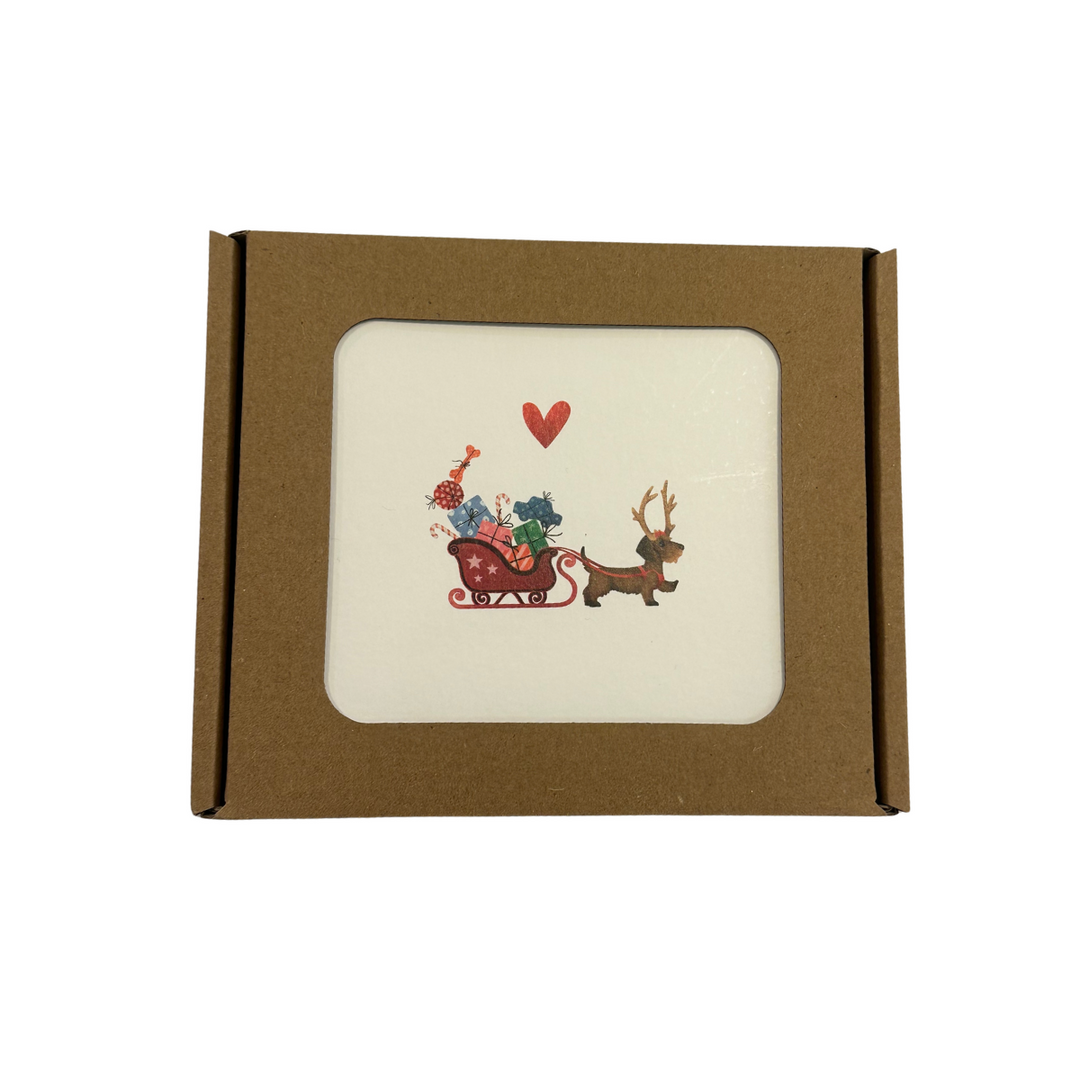 Boîte de Noël Yon 5 avec un teckel tirant un traîneau de cadeaux et un cœur rouge sur la carte du dessus