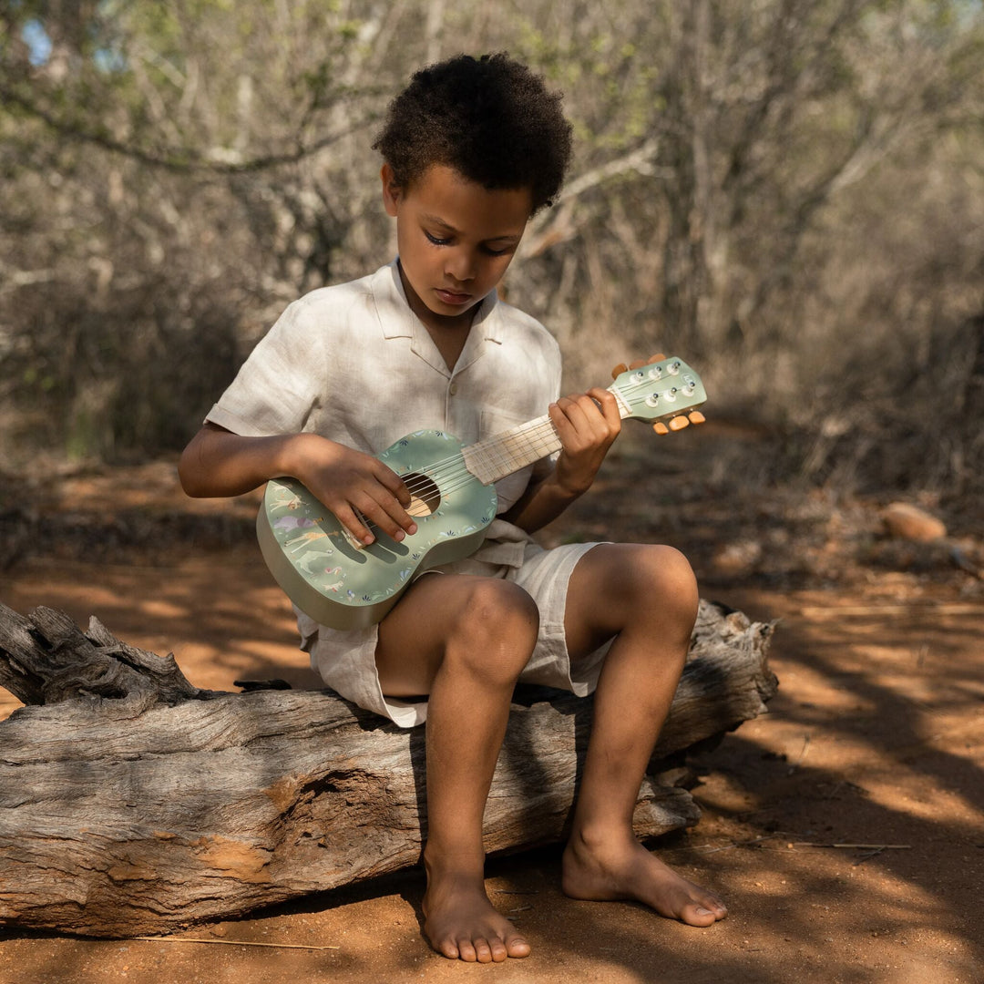 Kind speelt zittend op een boomstam op de groene Little Dutch Safari Friends gitaar