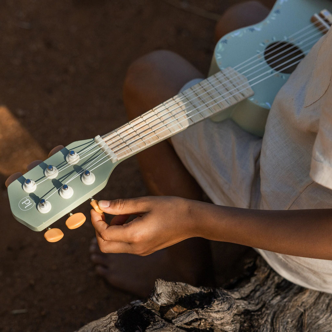 Kind stemt de snaren van de groene Little Dutch Safari Friends gitaar