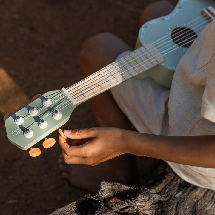 Kind stemt de snaren van de groene Little Dutch Safari Friends gitaar