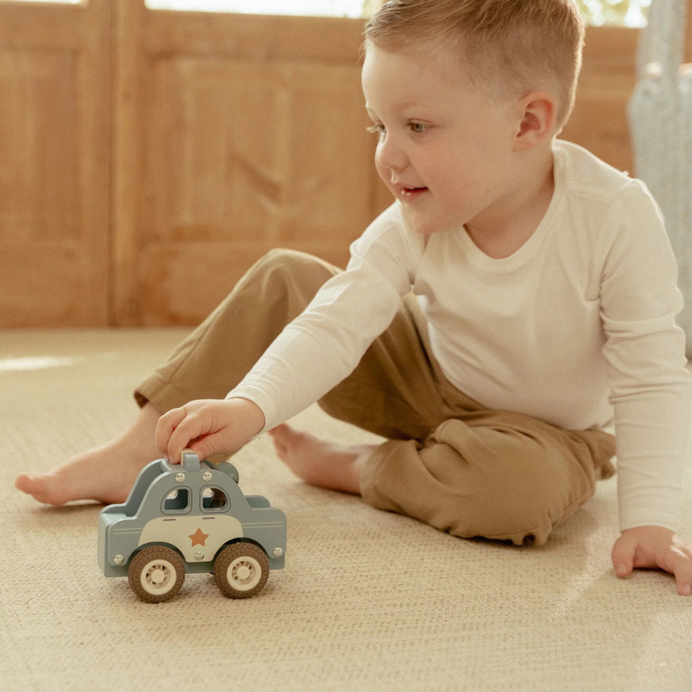 Kind beim Rollen des Little Dutch-Polizeiautos über einen Teppich