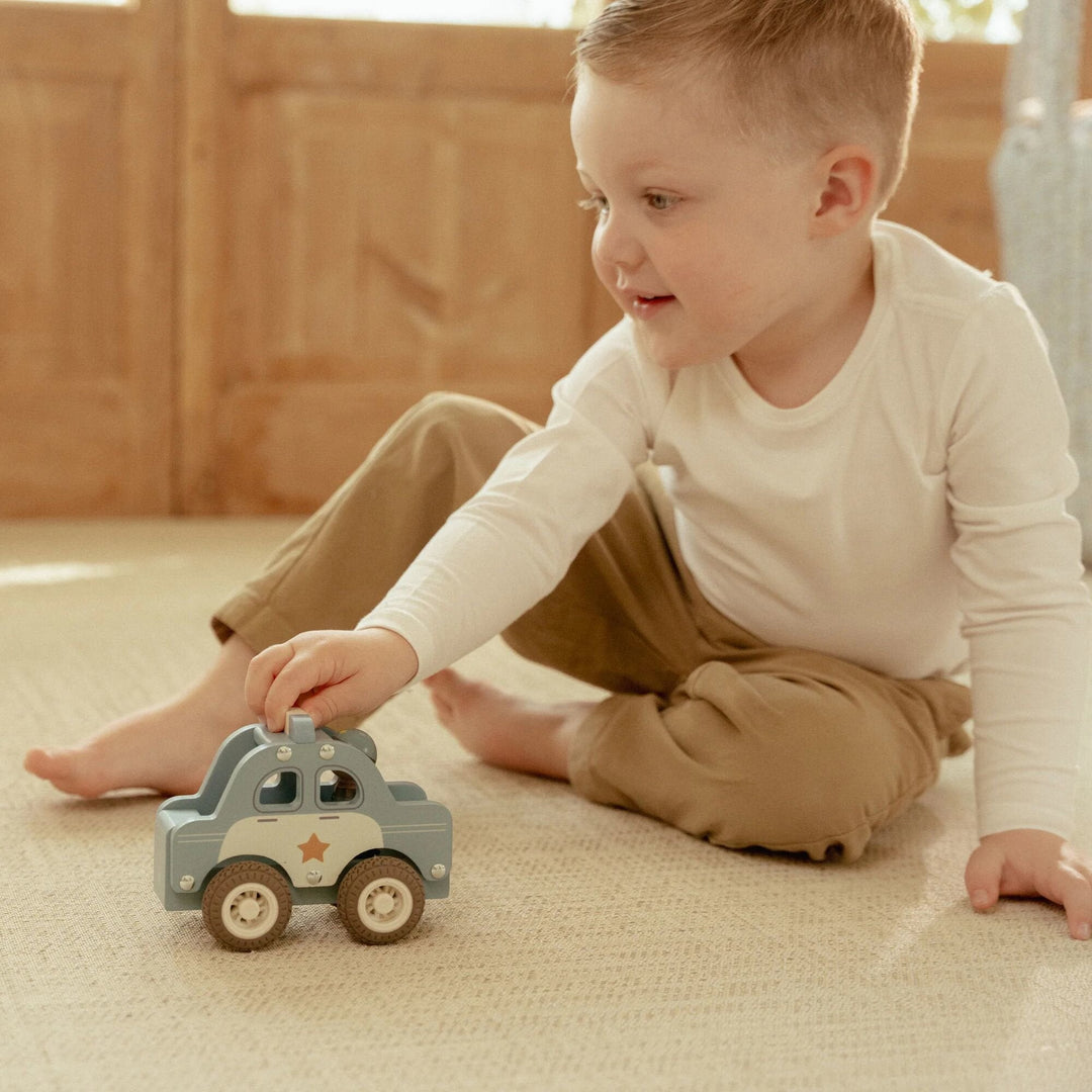 Kind beim Rollen des Little Dutch-Polizeiautos über einen Teppich