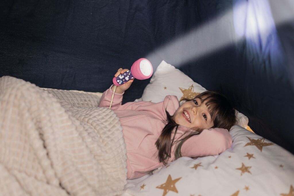 Kind benutzt die Einhorn-Taschenlampe beim Lesen im Bett.