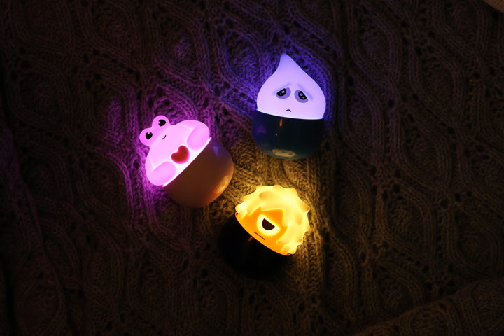 Drei leuchtende Eggy Monsters-Lichter in Rosa, Lila und Gelb in einem hohlen Baum.