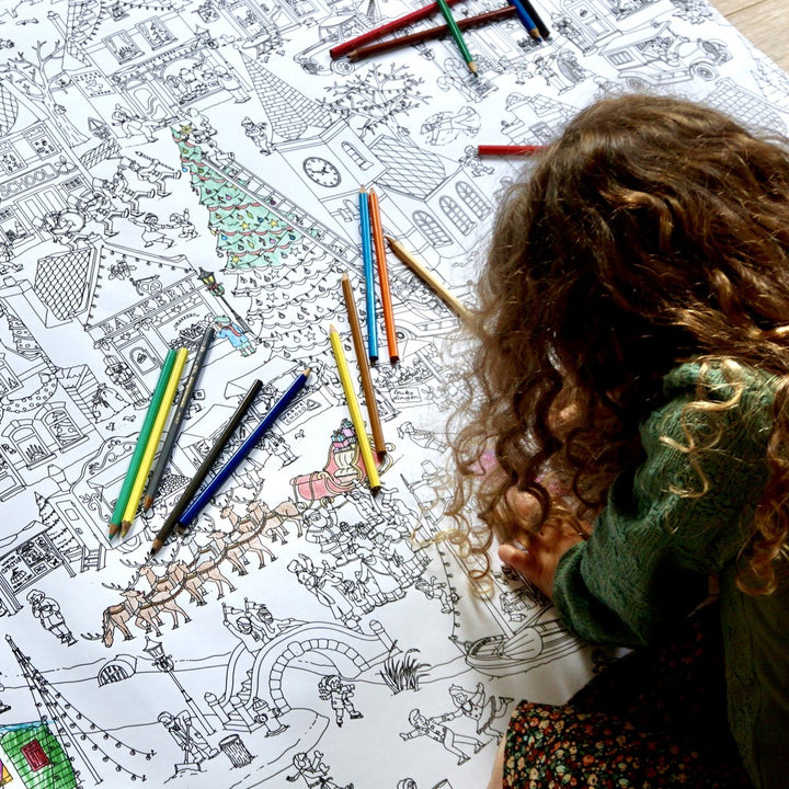 Child in a green jumper colouring part of the winter village with coloured pencils.