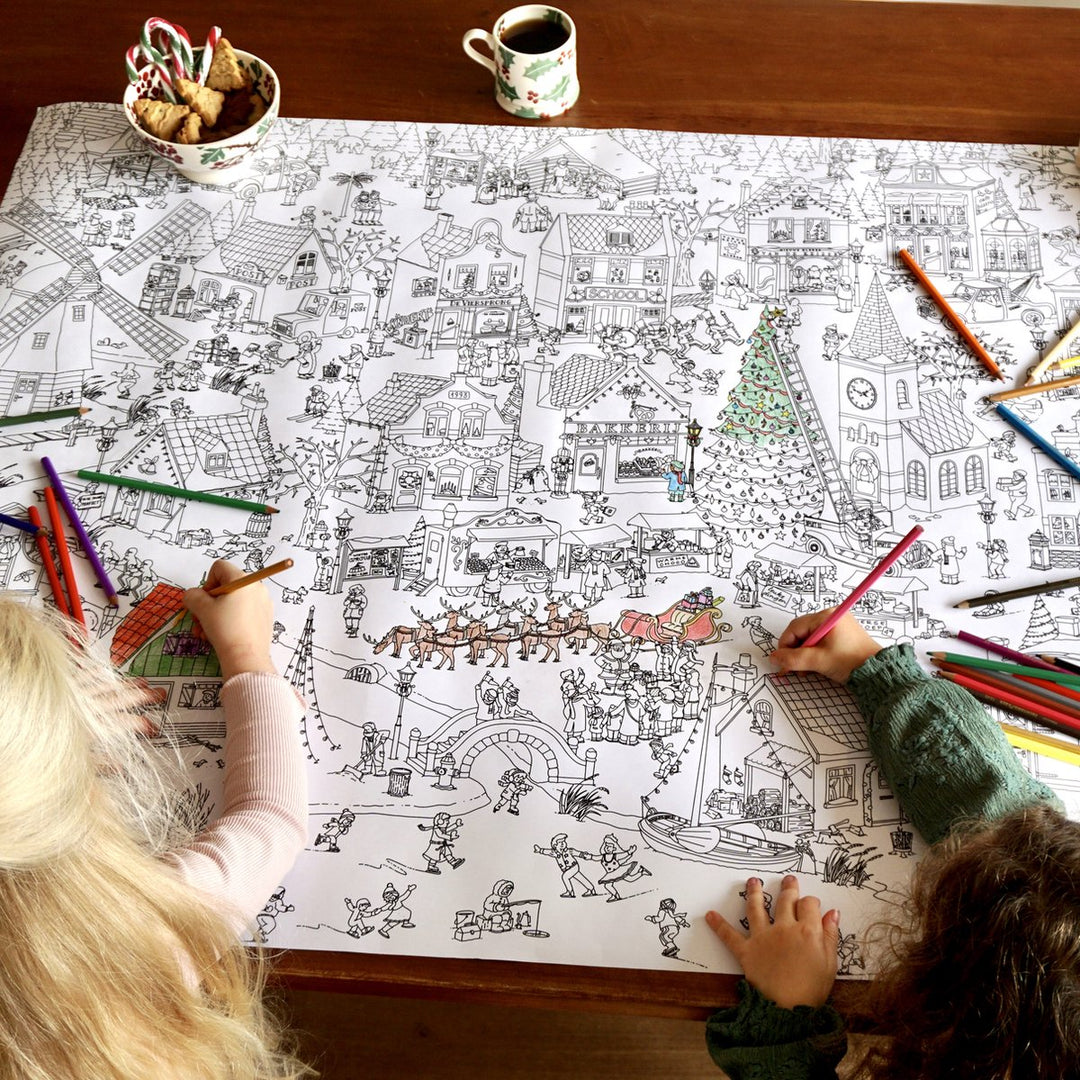 Two children working on the large winter colouring poster on a table, with pencils along the edge.