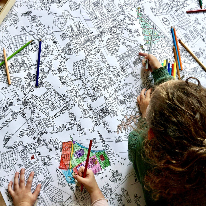 Detail of the winter village being coloured in, with loose coloured pencils on the poster.