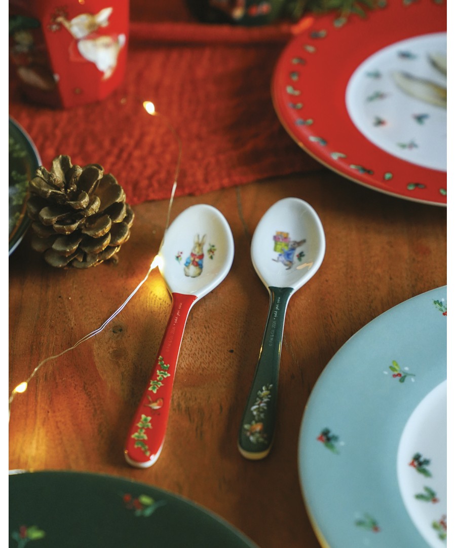Rode en groene Peter Rabbit kerstlepels naast kerstservies op een houten tafel