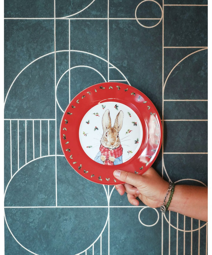 Rood Peter Rabbit kerstbord van Petit Jour in een hand voor een tegelwand